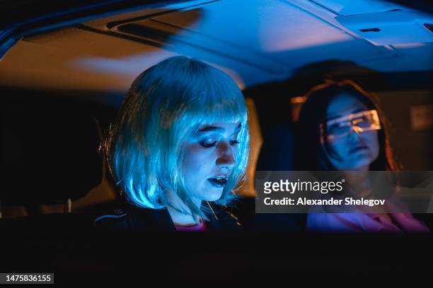 female portrait of two women with blue hairstyle who sitting on the backseat of car. neon light concept photography, girl is passenger, futuristic photo with color lighting indoors the vehicle - cyber punk girl stock pictures, royalty-free photos & images