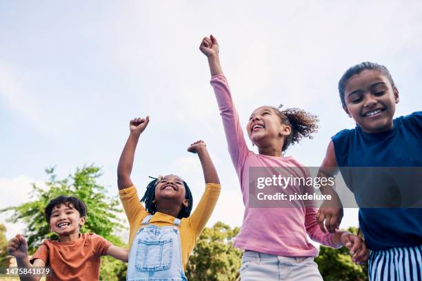 children, freedom and energy with friends cheering together outdoor while having fun during the day. kids, energy or diversity with a girl and boy group playing or bonding outside in summer - kinder stockfoto's en -beelden