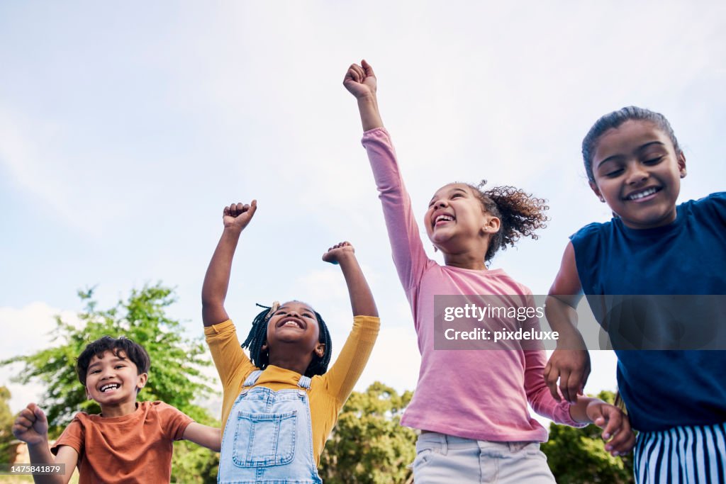 Children, freedom and energy with friends cheering together outdoor while having fun during the day. Kids, energy or diversity with a girl and boy group playing or bonding outside in summer