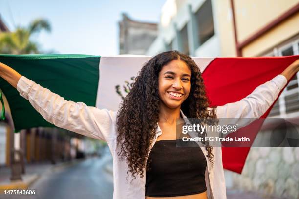 portrait of young woman holding a mexican flag on the street - cinco de mayo stockfoto's en -beelden