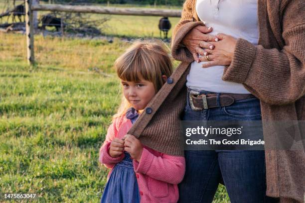 cute girl looking away while standing with mother on field - verlegen stockfoto's en -beelden