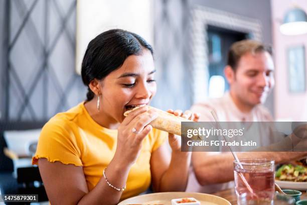 junge frau isst einen burrito in einem restaurant - tortilla sandwich stock-fotos und bilder