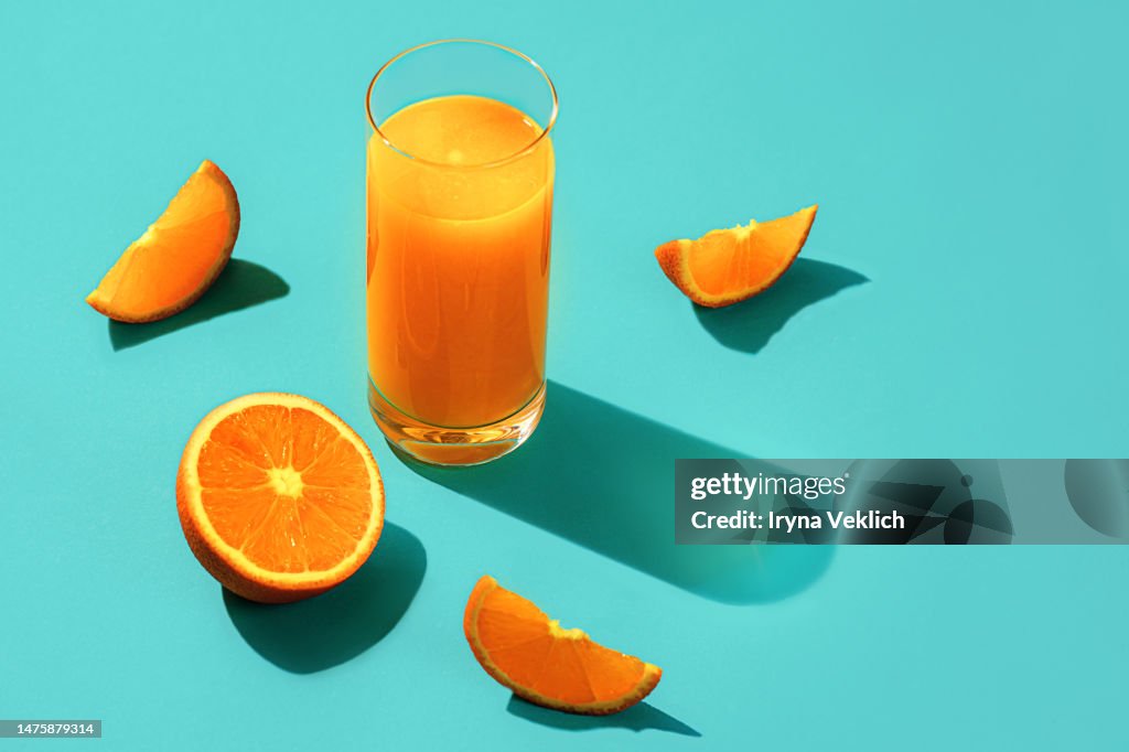Concept of Vitamin C with slices of orange fruit, glass of orange juice and shadows on a turquoise green background.