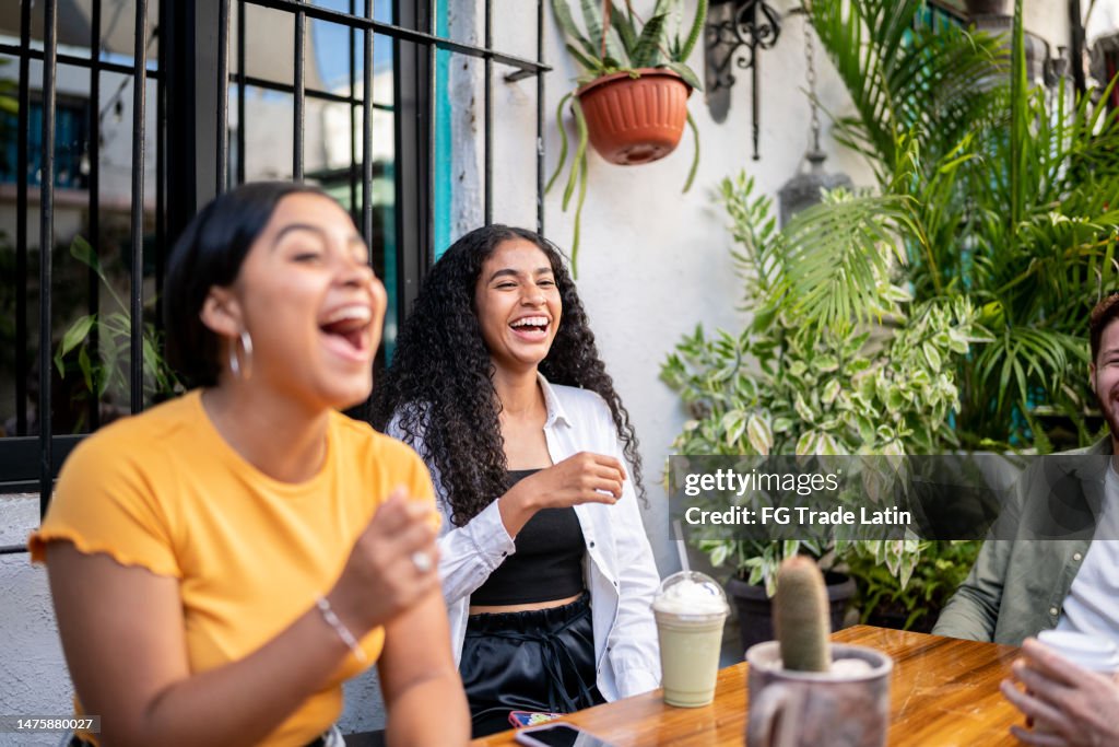 Young woman laughing while talking with her friends sitting at a table