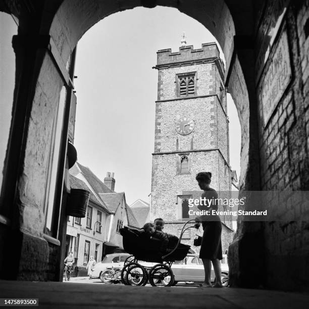 Woman pushing a pram with two children in it walks past an archway opposite The Clock Tower on Market Place, St Albans, Hertfordshire, May 4th 1960.