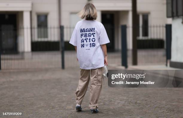 Victoria Thomas seen wearing Hernameis white oversized cotton shirt with navy blue back print, gold jewelry, H&M beige cargo pants, white socks,...