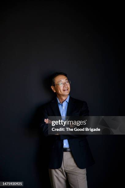 smiling man looking away while standing with arms crossed against black background - three quarter length stock pictures, royalty-free photos & images