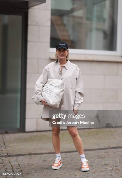 Victoria Thomas seen wearing Hernameis black logo cap, By Aylin Koenig beige oversized shirt, Hernameis beige printed shopper bag, The Wants x...