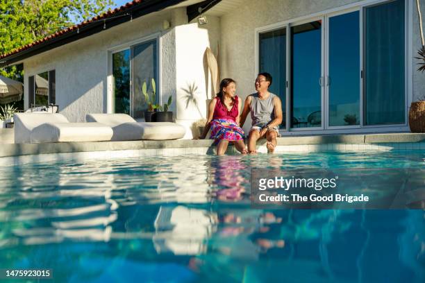 happy couple spending leisure time while sitting near swimming pool during vacation - home golden hour stock pictures, royalty-free photos & images