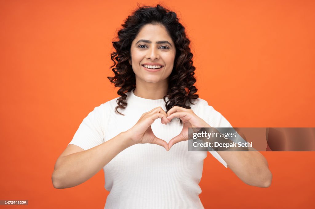 Photo of happy girl making demonstrating heart on chest on orange background, stock photo