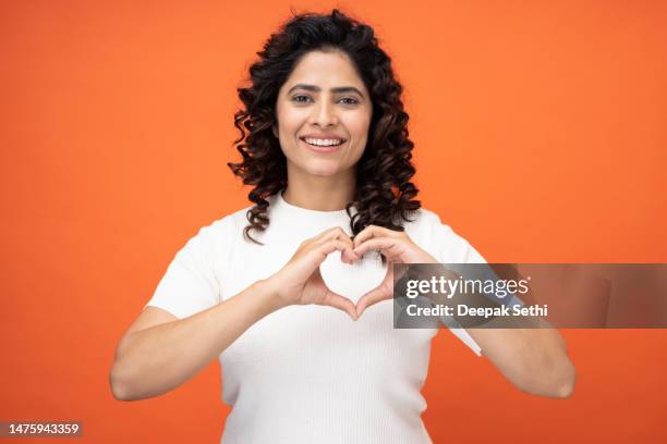 photo of happy girl making demonstrating heart on chest on orange background, stock photo - hands in heart shape stock pictures, royalty-free photos & images