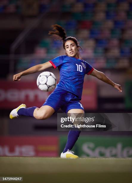 athletic female soccer midfielder winds her leg as she prepares to volley a soccer ball at the goal during a game - futbolistas fotografías e imágenes de stock