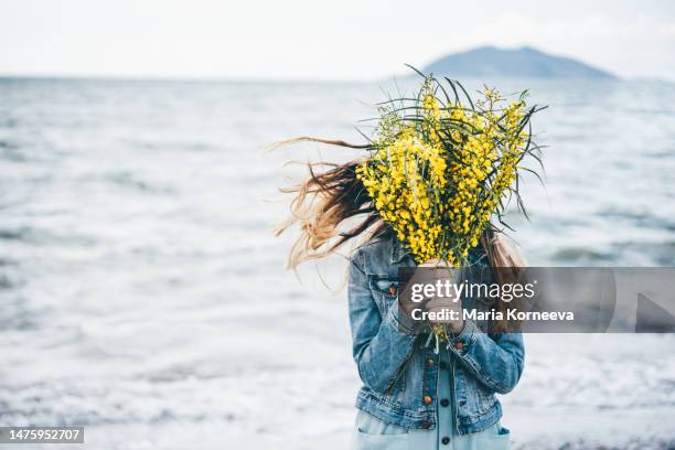 beautiful woman standing near the sea with yellow flowers mimosa. - acacia flowers stock pictures, royalty-free photos & images