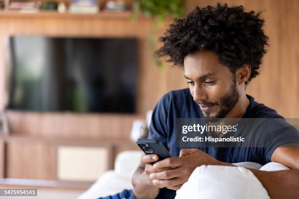 uomo che guarda i social media sul suo cellulare mentre si rilassa a casa - video on demand foto e immagini stock