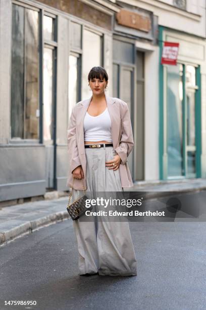 Gili Biegun wears pearl earrings, a pastel muted colored soft-shade tailored outfit, a blue denim bag by Dior, a light lilac pastel colored blazer...