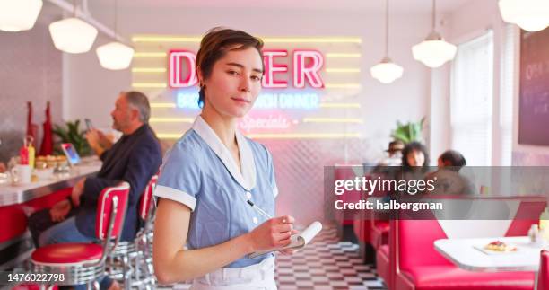 waitress holding notepad and looking in 1950s styled diner - waitress booth stock pictures, royalty-free photos & images