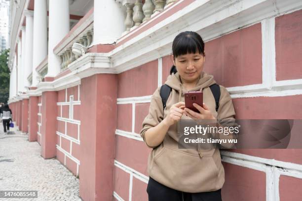 eine touristin lehnte an der straßenmauer und schaute auf ihr handy - portraits fun mobile wall stock-fotos und bilder