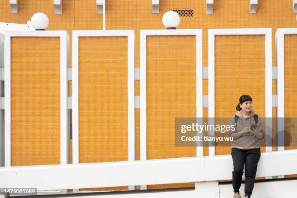 eine touristin sitzt an der straßenmauer, ruht sich aus und schaut auf ihr handy - portraits fun mobile wall stock-fotos und bilder