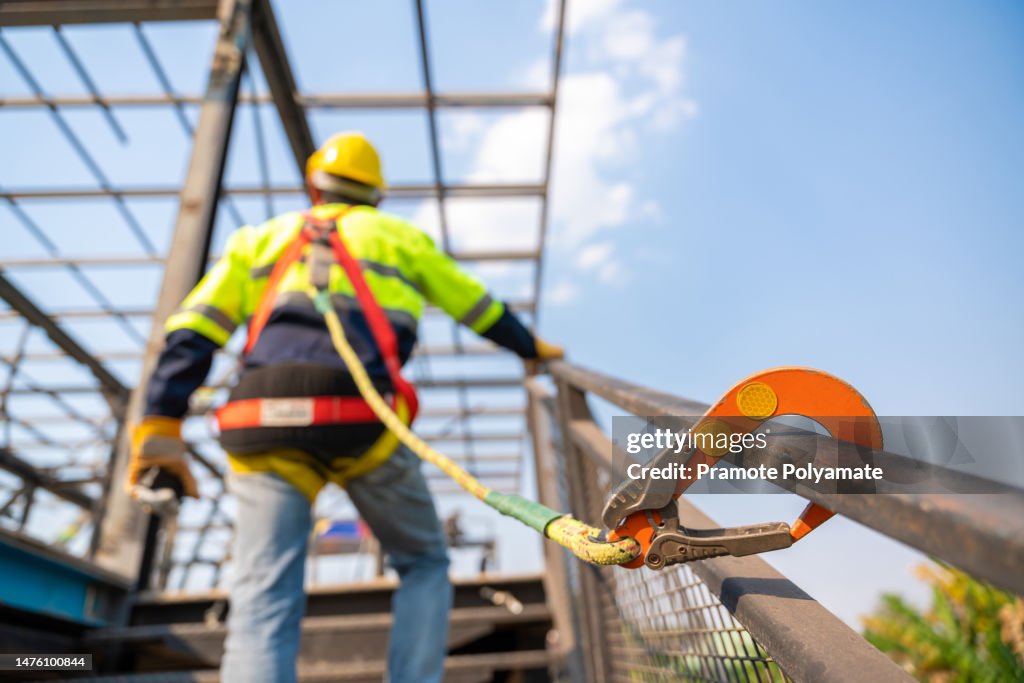 A construction worker working at height, Construction workers are working on steel roof trusses with Fall arrestor device for worker with hooks for safety body harness on the construction site.