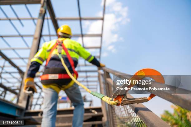 a construction worker working at height, construction workers are working on steel roof trusses with fall arrestor device for worker with hooks for safety body harness on the construction site. - andaime imagens e fotografias de stock