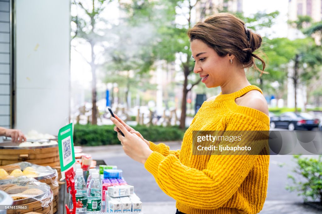 Young female customer using digital payment method, scanning QR code with smartphone