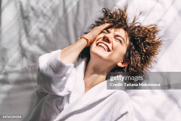 beautiful cheerful woman in a white terry bathrobe on the bed in the morning, top view. - bathrobe stock pictures, royalty-free photos & images