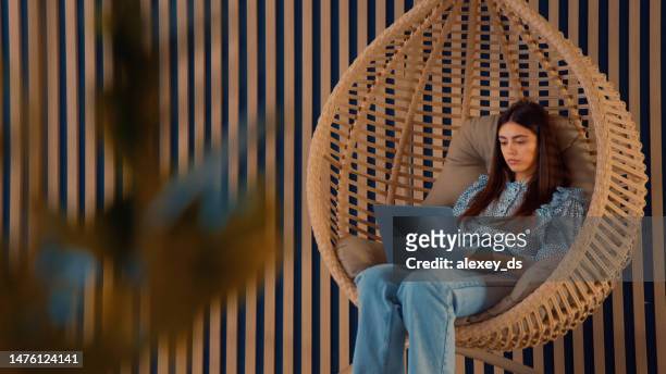 junge frau arbeitet, während sie in einem gemütlichen hängenden schaukelstuhl sitzt - bubble chair stock-fotos und bilder