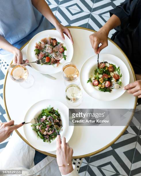 three women are having lunch in restaurant. three plates of salad and glasses of white wine on round white table. light lunch. italian restaurant. healthy food. fitness menu. top view - freshness concept stock pictures, royalty-free photos & images