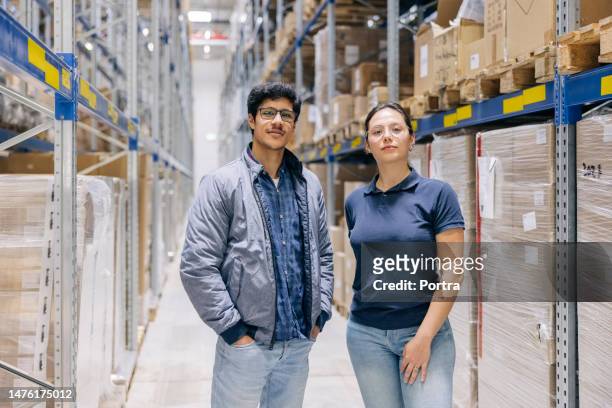 porträt von zwei lagerarbeitern, die an regalen stehen - baumarkt mitarbeiter stock-fotos und bilder