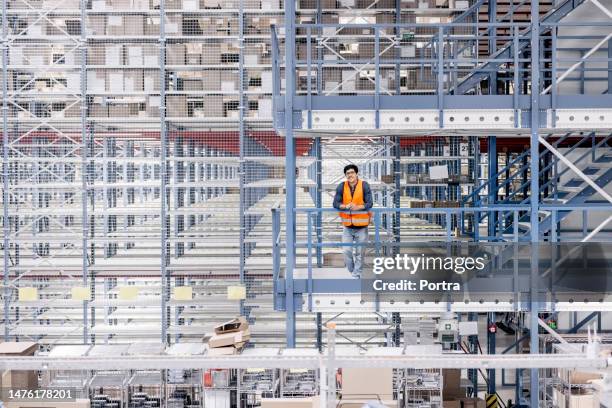 portrait of smiling young warehouse worker standing at balcony railing - lean manufacturing stockfoto's en -beelden