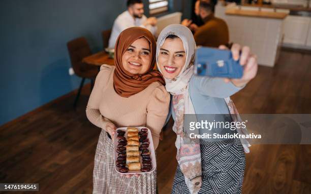 two smiling muslim women taking selfies with food for ramadan feast - ramadan giving stockfoto's en -beelden