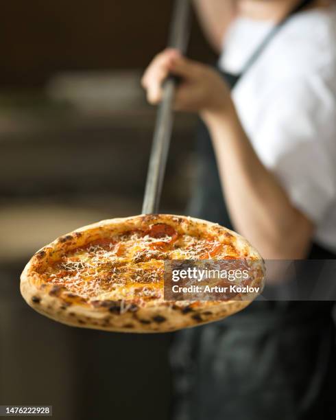 freshly baked pizza on baking sheet. cook takes pizza out of oven. pizza with pepperoni and cheese baked in oven. italian cuisine. blurred background. front view. soft focus. - pizza chef stock pictures, royalty-free photos & images