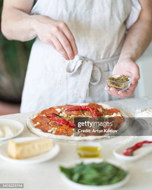 unbaked pizza and ingredients on table. process of making pizza. pizzaiollo makes toppings. spices for pizza. pizza with pepperoni, cheese, pepper and tomato sauce. front view. soft focus - tomato paste stock pictures, royalty-free photos & images