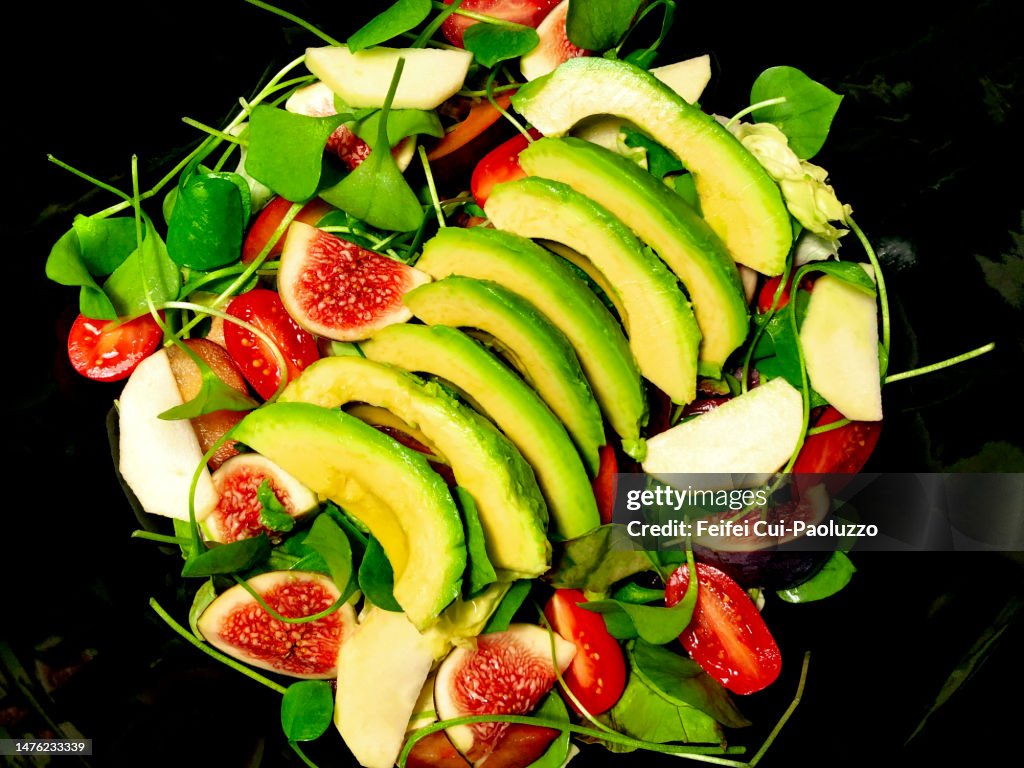 Close-up of fresh salad with slice of avocado, fig, apple, miner's lettuce, tomato