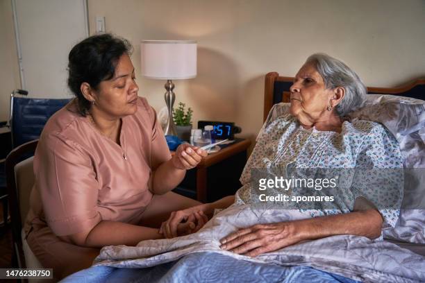 krankenschwester misst körpertemperatur für eine hispanische ältere frau zu hause mit digitalem messgerät - hot nurse stock-fotos und bilder