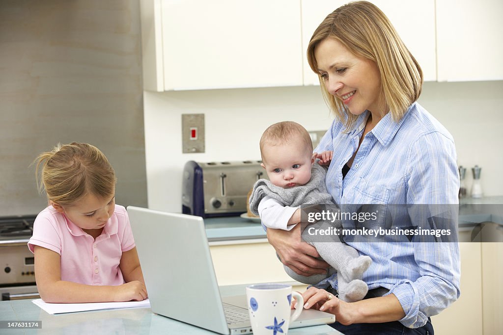 Madre con bambini utilizzando un computer portatile in cucina
