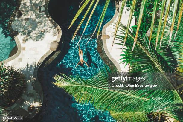 aerial drone view of woman floating on water surface in luxury pool in tropical garden - swimming pool stock pictures, royalty-free photos & images