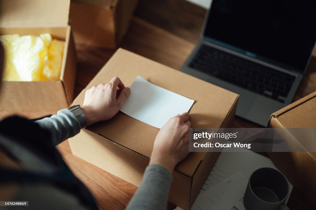 Close-up of female hand attaching shipping labels onto parcel box