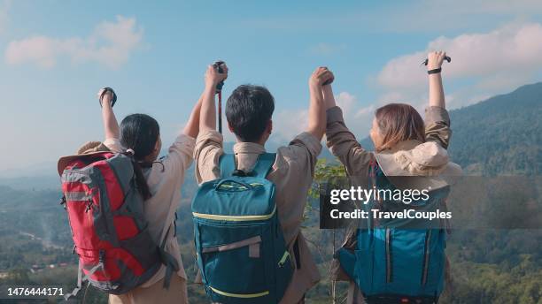 rear view three friends hikers with backpacks enjoying trekking day on mountain. carefree climbing tourists raised arms looking at horizon. freedom. success sport concept - womens champions day three stock pictures, royalty-free photos & images