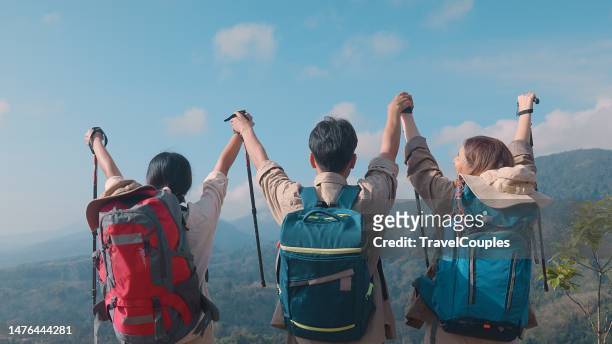 rear view three friends hikers with backpacks enjoying trekking day on mountain. carefree climbing tourists raised arms looking at horizon. freedom. success sport concept - womens champions day three stock pictures, royalty-free photos & images