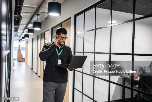 mature man walking while use laptop in the corridor at office - employee badge stock pictures, royalty-free photos & images