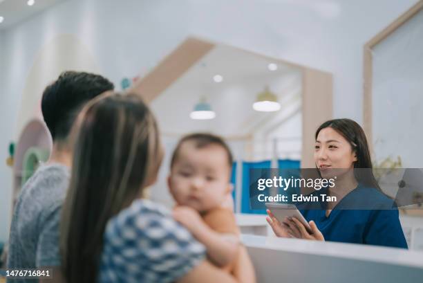 asian chinese female pediatric nurse helping patient baby parents to register at counter in clinic with digital tablet fill up e-form - southeast asian ethnicity stock pictures, royalty-free photos & images