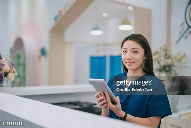 portrait asian chinese female nurse at lobby receptionist counter registration looking at camera smiling - asian receptionist stock pictures, royalty-free photos & images