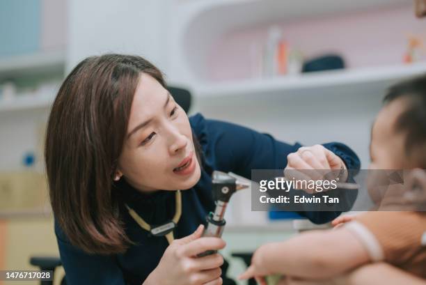 pediatra chinesa asiática examinando garganta de menino com depressor de língua em sua clínica - asian baby - fotografias e filmes do acervo