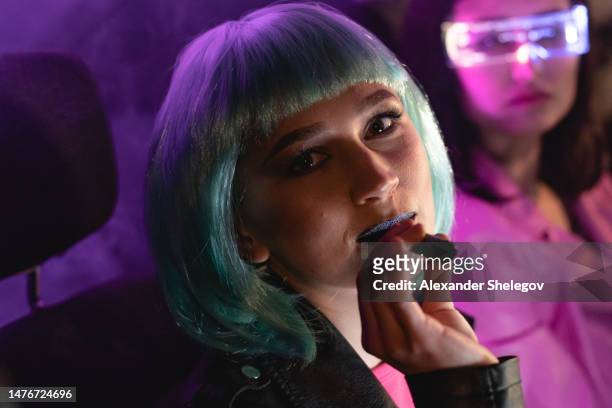 female portrait of two women who wear futuristic glasses and using vape for smoking indoors the car. film noir style and cyberpunk concept photography with neon light, girl vaping with electronic cigarette - magenta car stock pictures, royalty-free photos & images