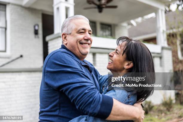 portrait of senior couple in front of suburban home - baby boomer photos et images de collection