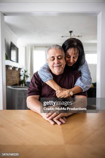 portrait of senior couple embracing in dining room - couple lifestyle jean stock pictures, royalty-free photos & images