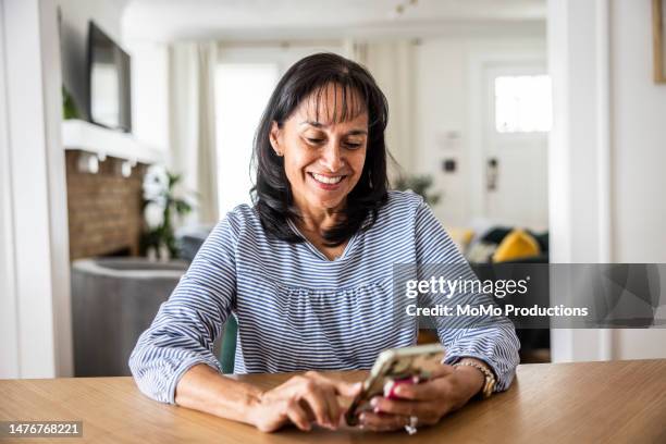senior woman using smartphone in dining room - zwart haar stockfoto's en -beelden