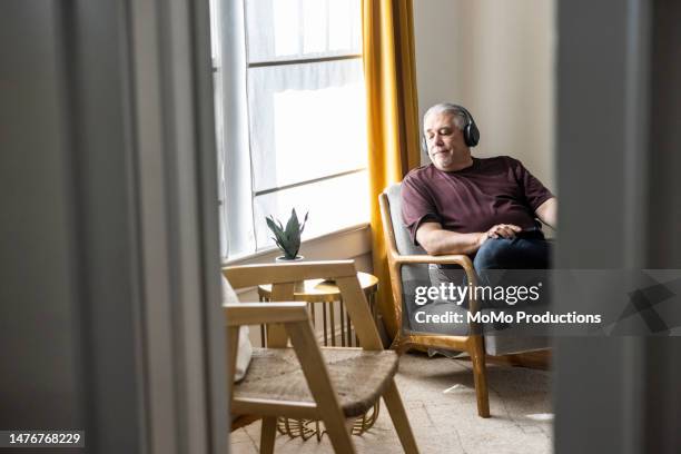 senior man listening to wireless headphones and looking out window - 60 64 jahre stock-fotos und bilder