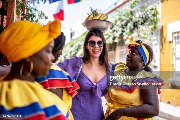 donna turistica che mette la ciotola di frutta in testa con palenqueras sulla strada a cartagena, colombia - cartagena foto e immagini stock